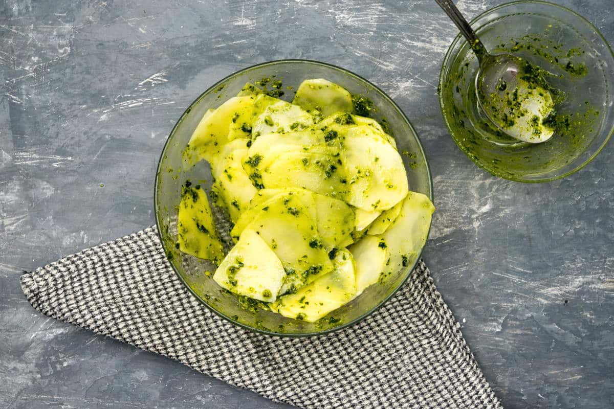 Sliced potatoes and basil pesto in a glass bowl.