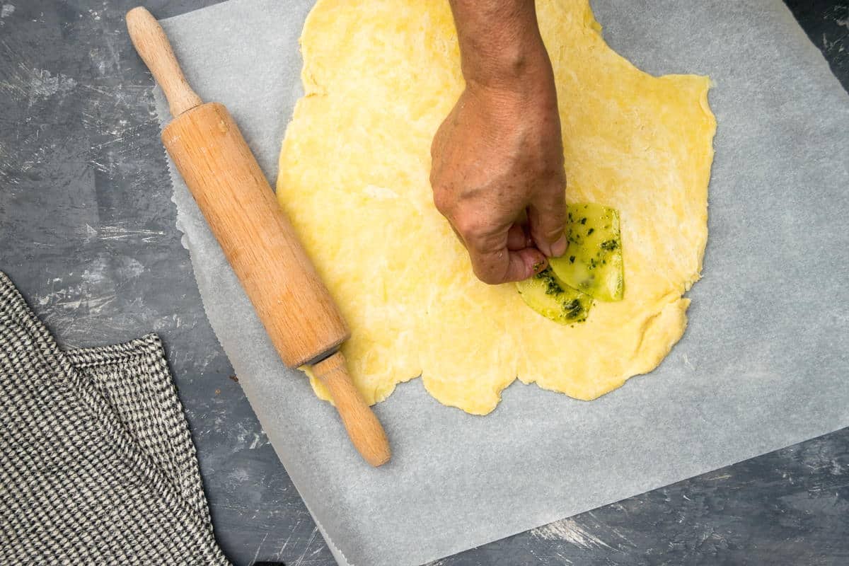 Pastry dough on parchment paper with a rolling pin and some potato slices.