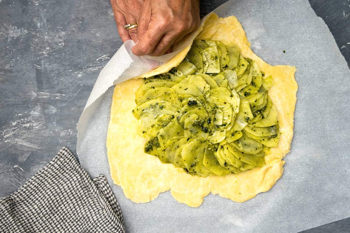 Rolled out pastry on parchment paper with potato slices in the center.