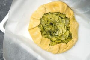 Galette pastry dough on parchment paper with potato slices in the center.