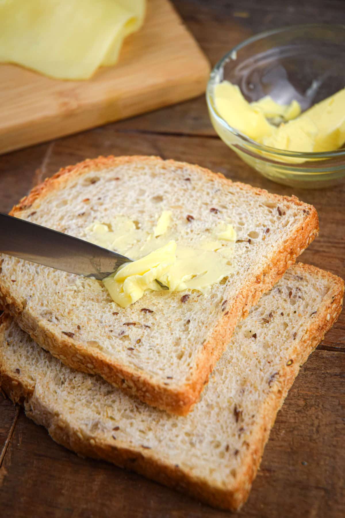 A knife buttering a piece of multigrain bread.