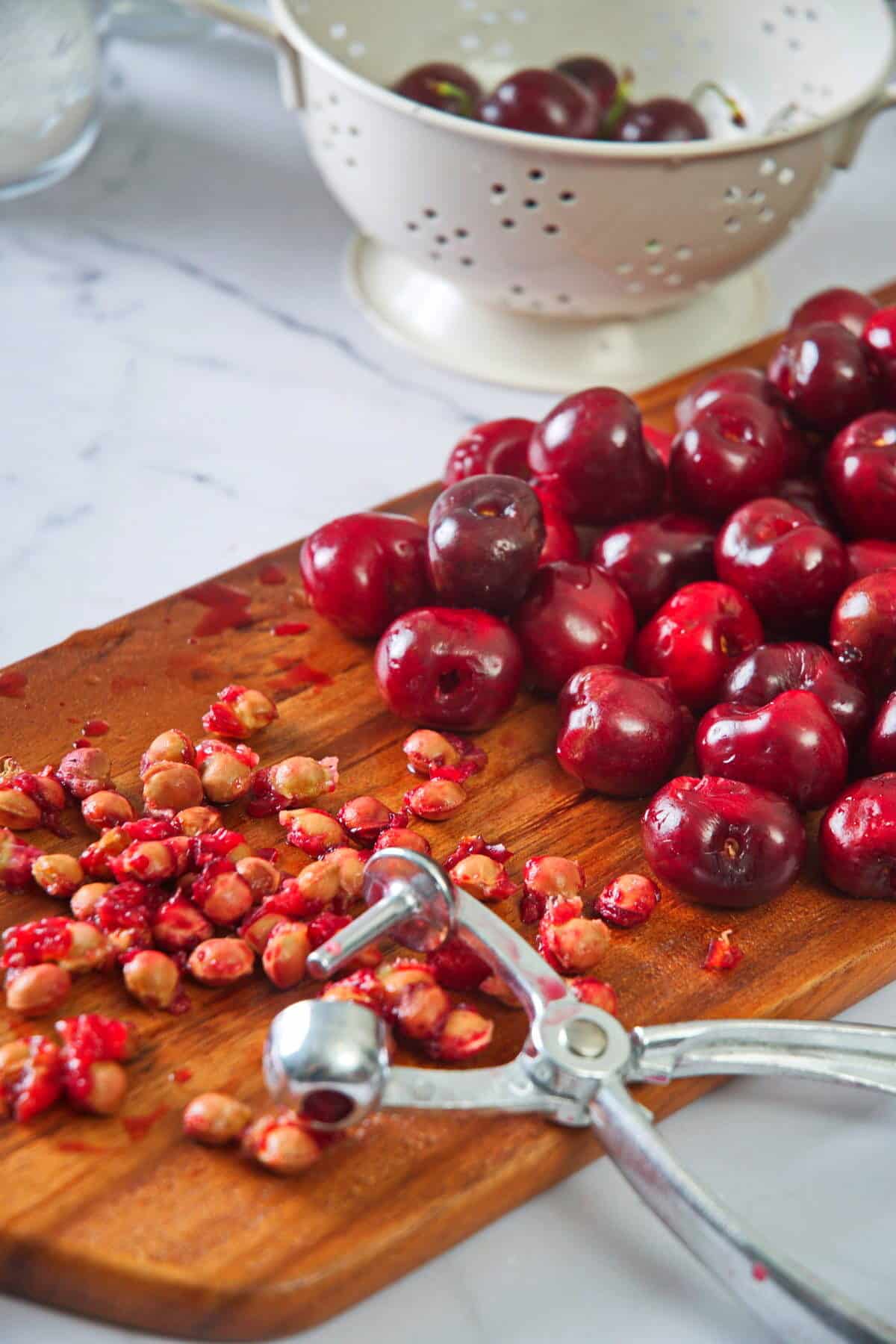 Pitted cherries and a cherry pitter on cutting board.