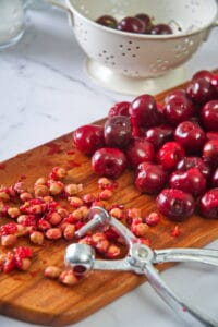 Pitted cherries and a cherry pitter on cutting board.