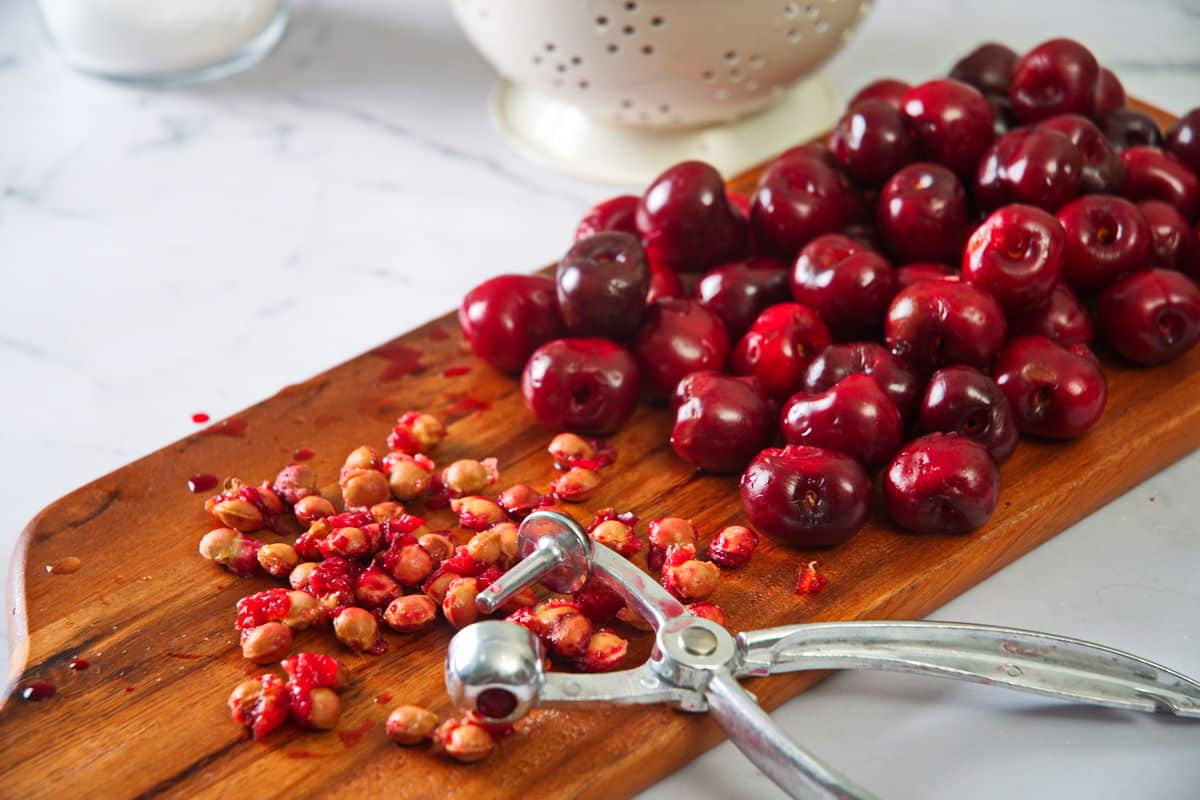 Pitted cherries and a cherry pitter on cutting board.