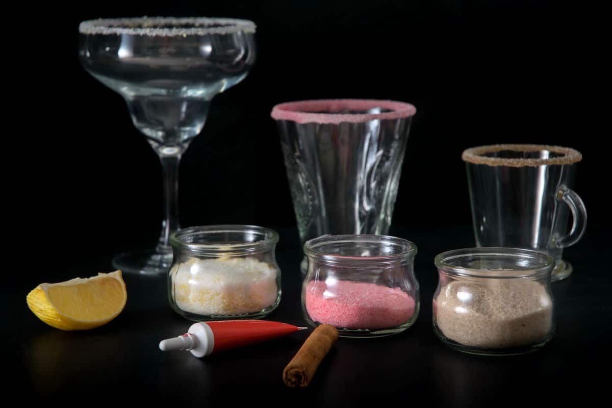 Sugar rim flavors in 3 jars with rimmed glasses in the background.
