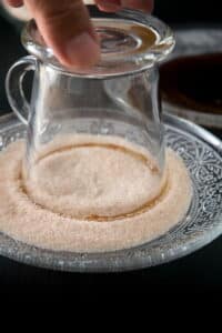 A clear glass coffee mug dipped into a plate of cinnamon sugar.