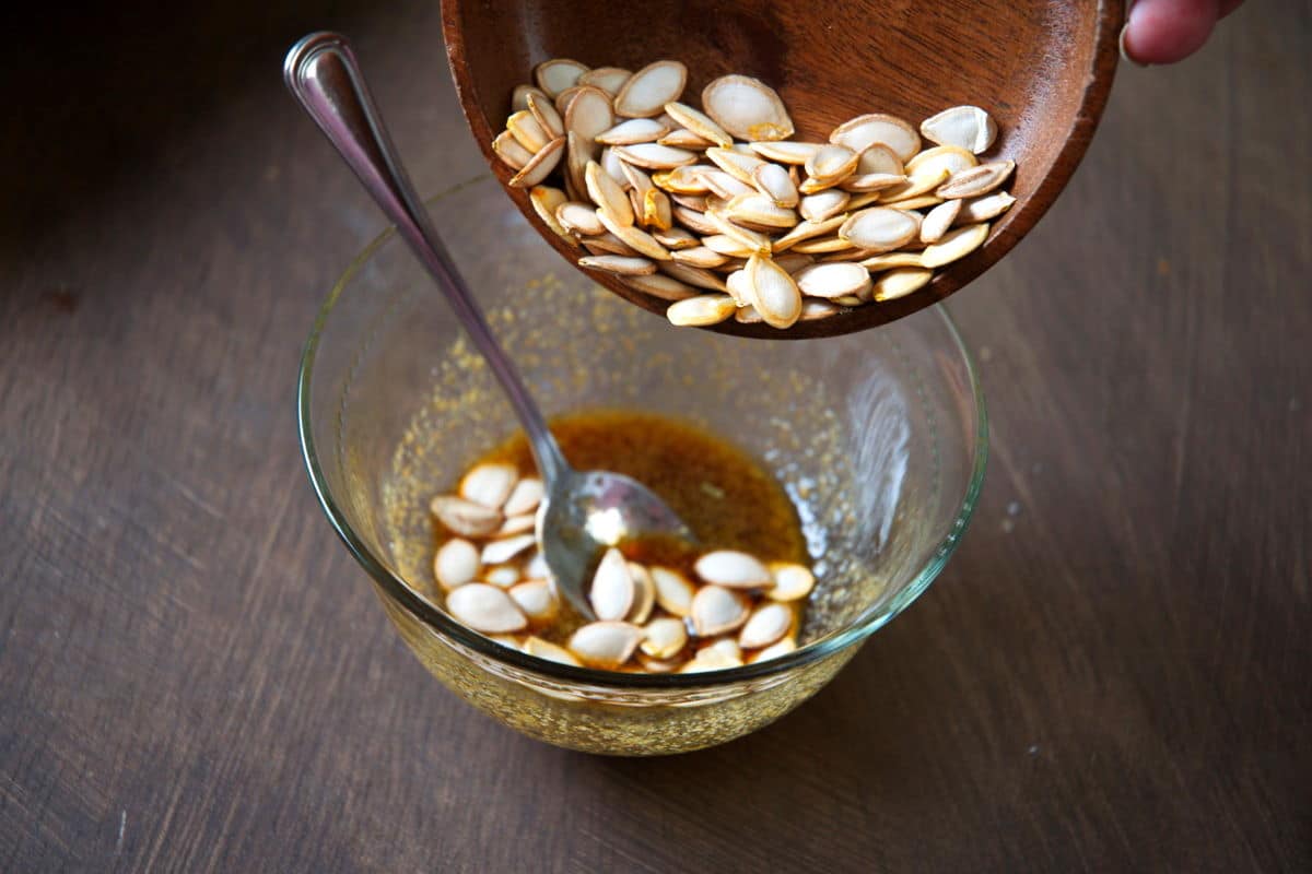 Butternut squash seeds in a bowl with a brown sugar and soy mixture.
