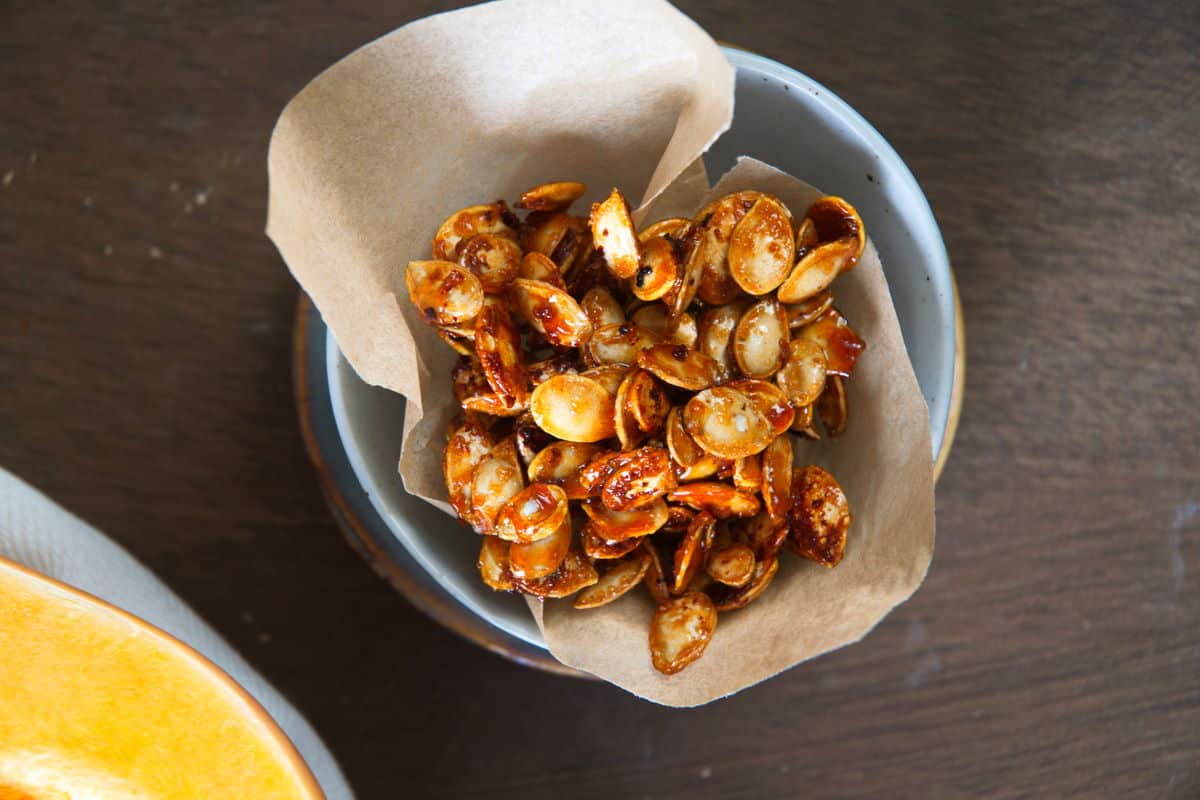 Roasted butternut squash seeds in a small blue bowl with parchment paper.