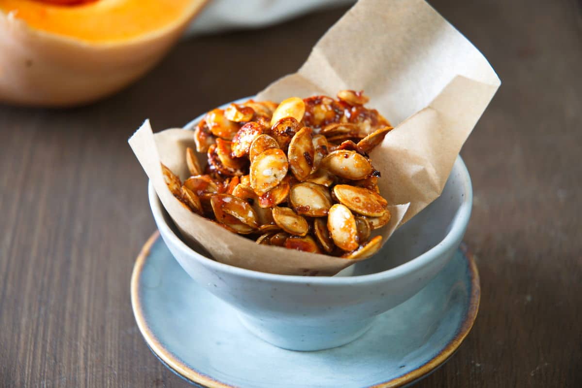 Roasted butternut squash seeds in a small blue bowl with parchment paper.