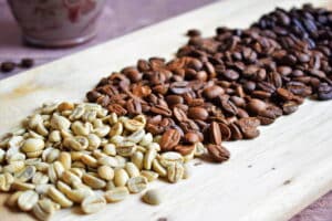 Green and brown coffee beans on wooden serving board.