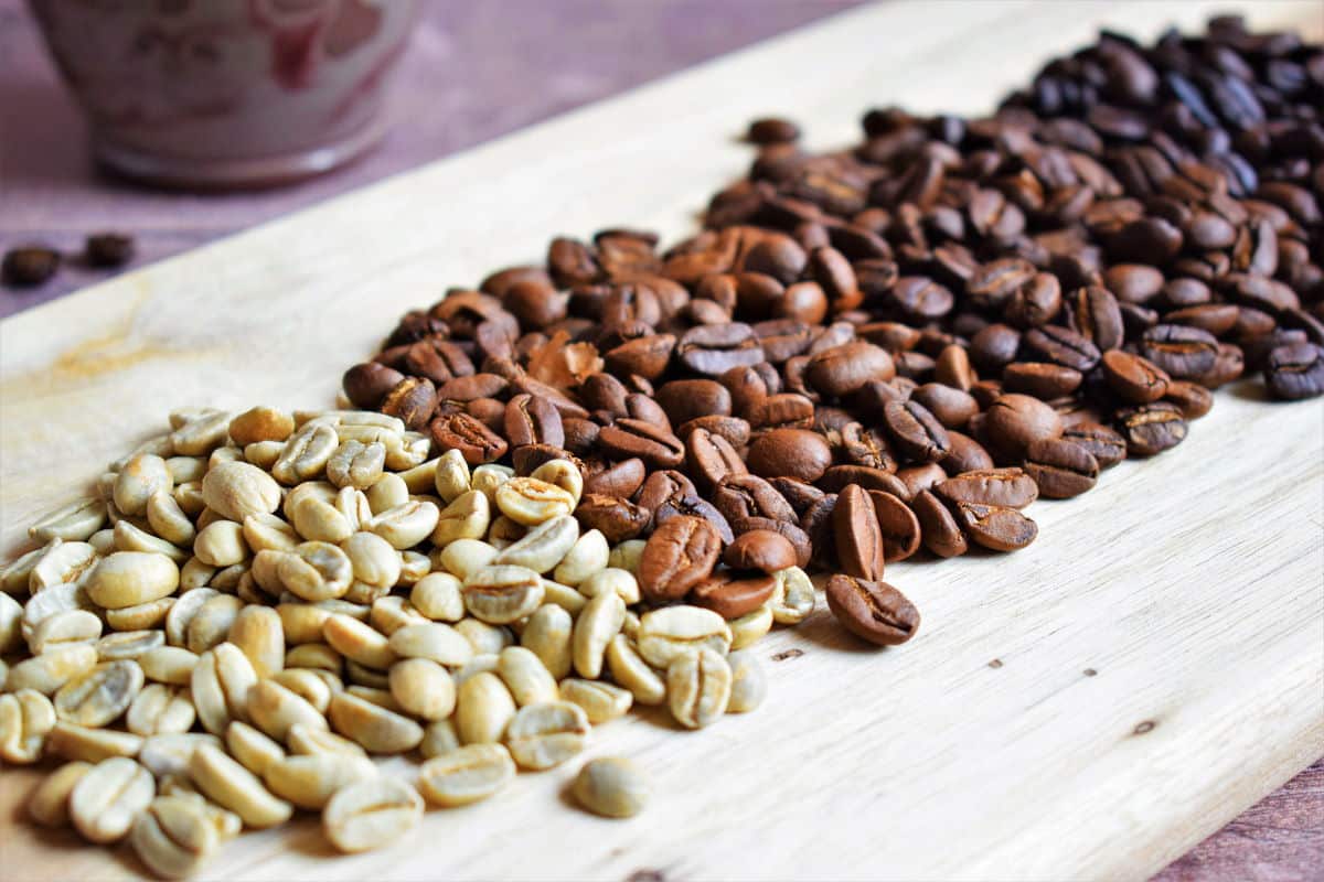 4 different roasts of coffee beans on wooden serving board.