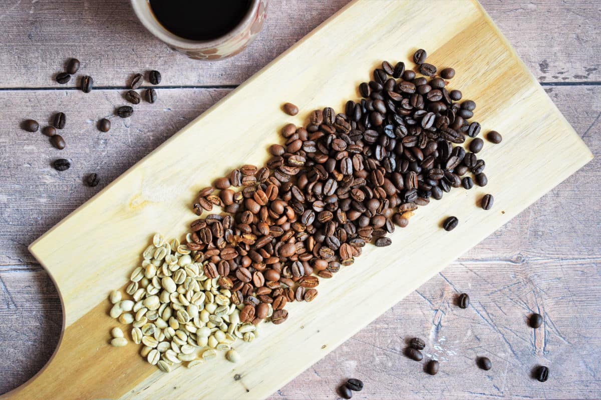 Green and brown coffee beans on wooden serving board.