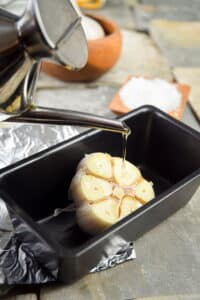 Head of garlic in pan with olive oil.