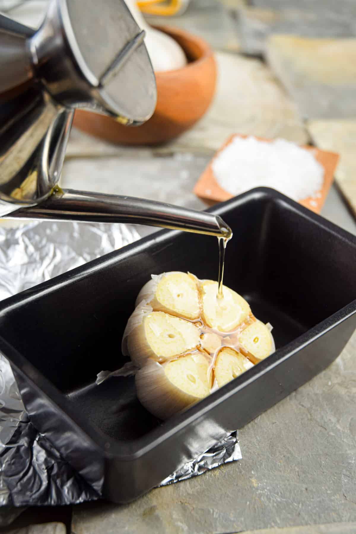 Head of garlic in pan with olive oil.