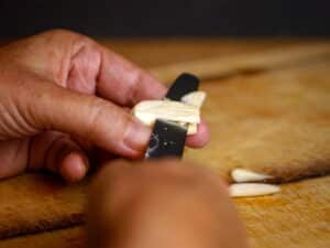 Woman's hands slicing garlic clove with small knife.