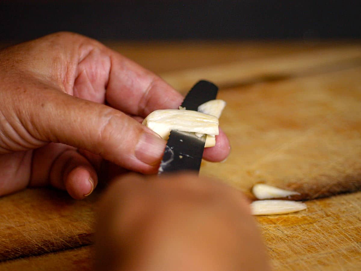 Woman's hands slicing garlic clove with small knife.