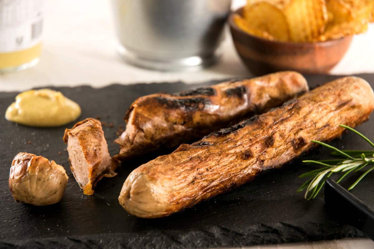 Grilled bratwurst sausage on charcoal cutting board.