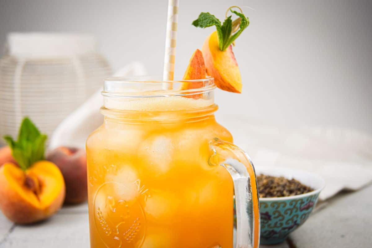 Iced peach green tea in glass with ice, straw and peach garnish.