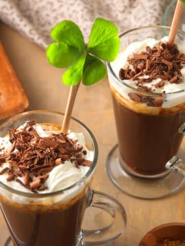 Irish coffee in coffee mug with 4 leaf clover, whipped cream and chocolate curls.
