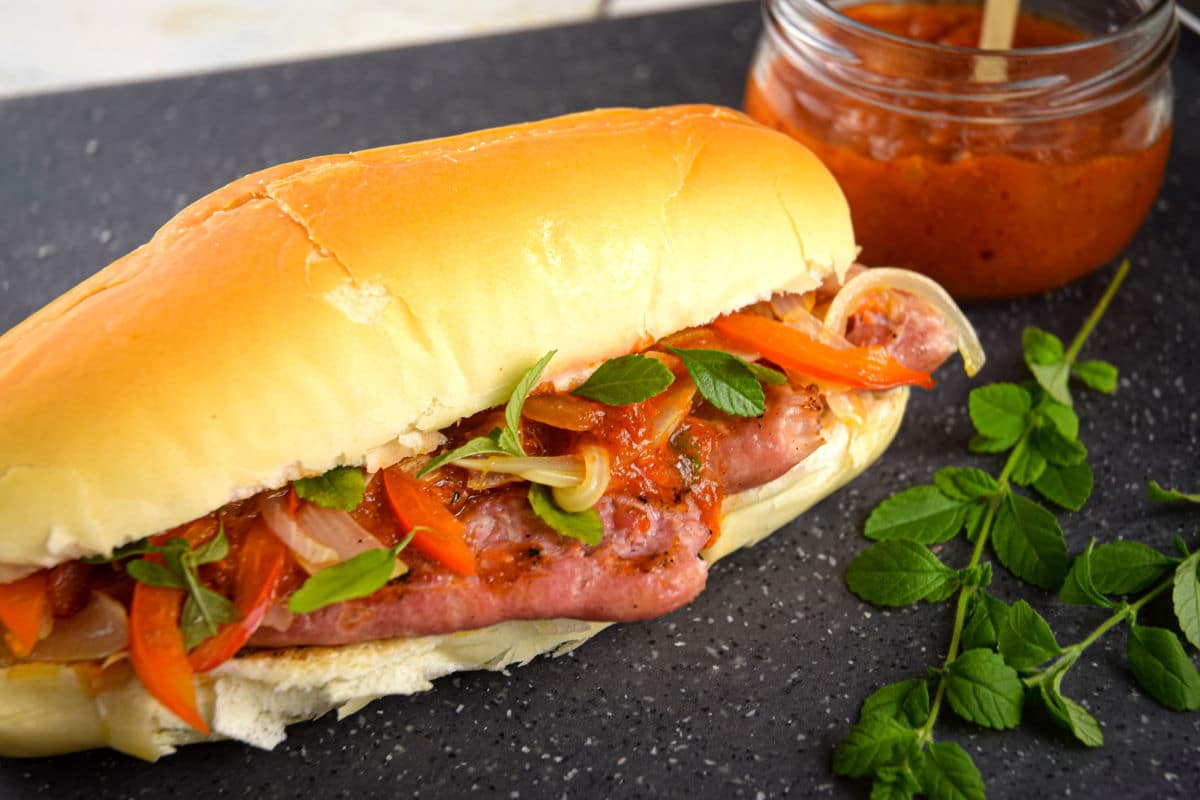 Italian sausage sandwich with fresh oregano and a jar of pepper sauce on the side.