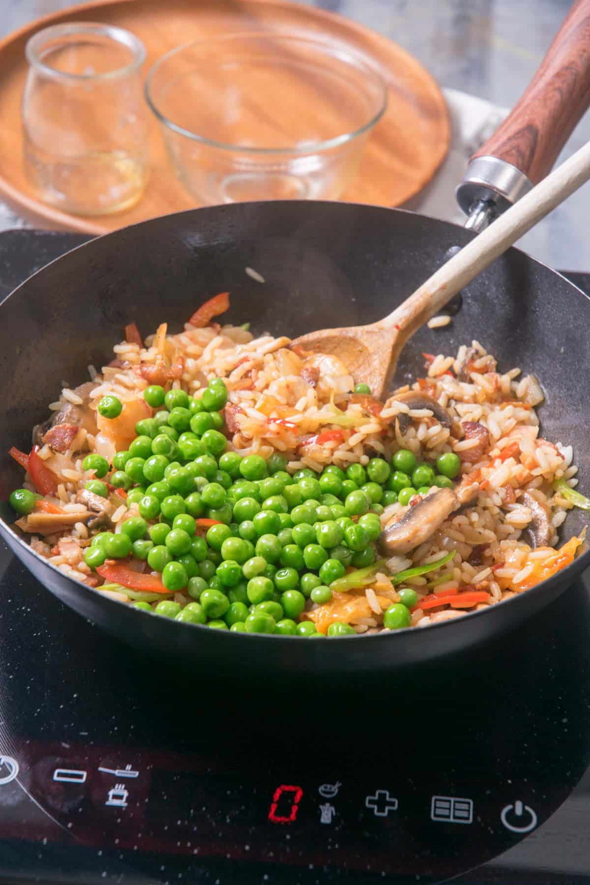 Kimchi bacon fried rice in frying pan with a wooden spoon on element.