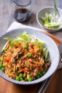 Kimchi bacon fried rice in bowl, with fork and knife on the side, sliced green onions in the background.