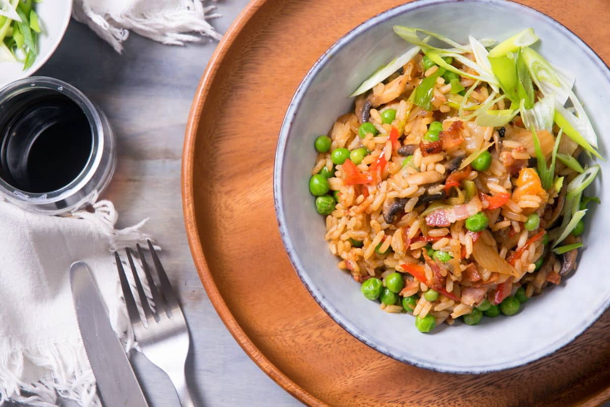 Kimchi bacon fried rice in bowl, with fork and knife on the side.
