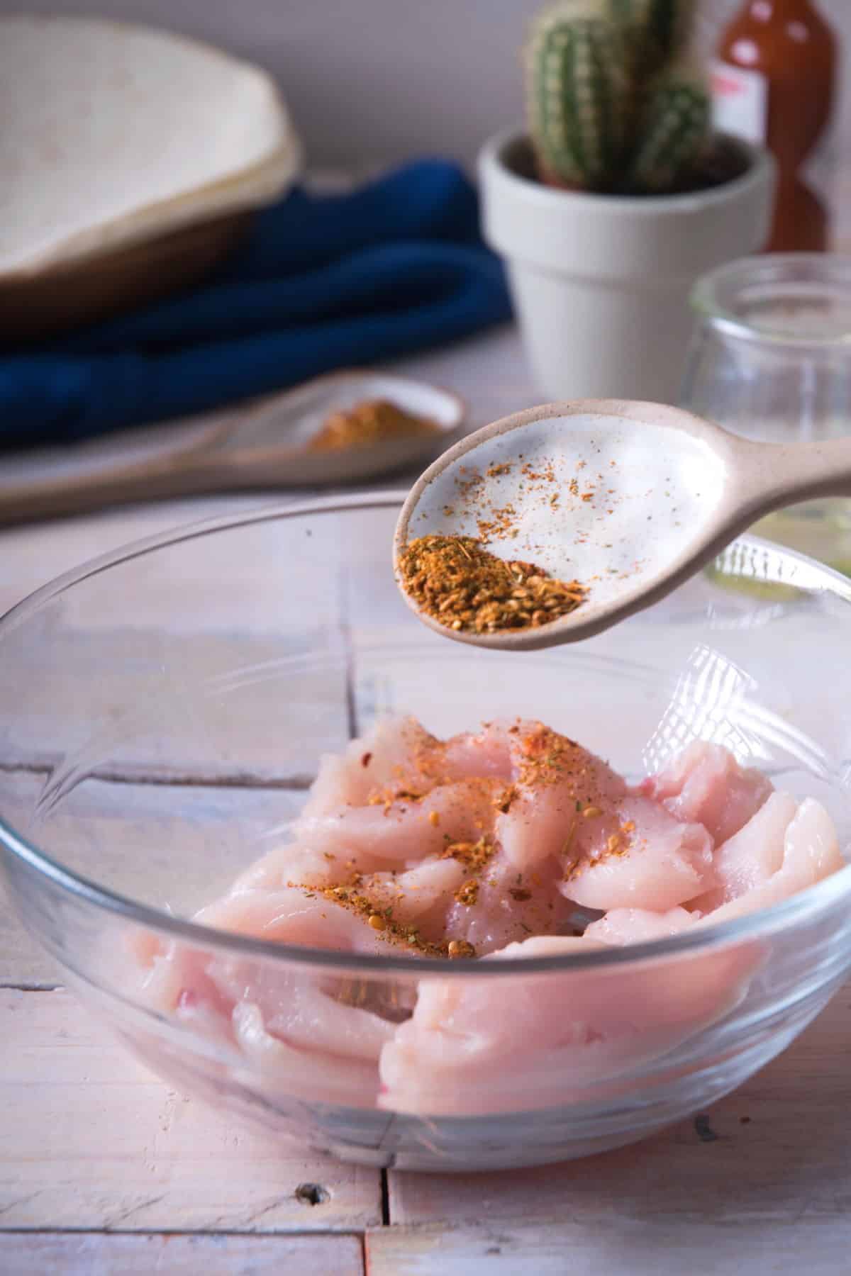 Raw chicken tenders in a bowl with Mexican spices.