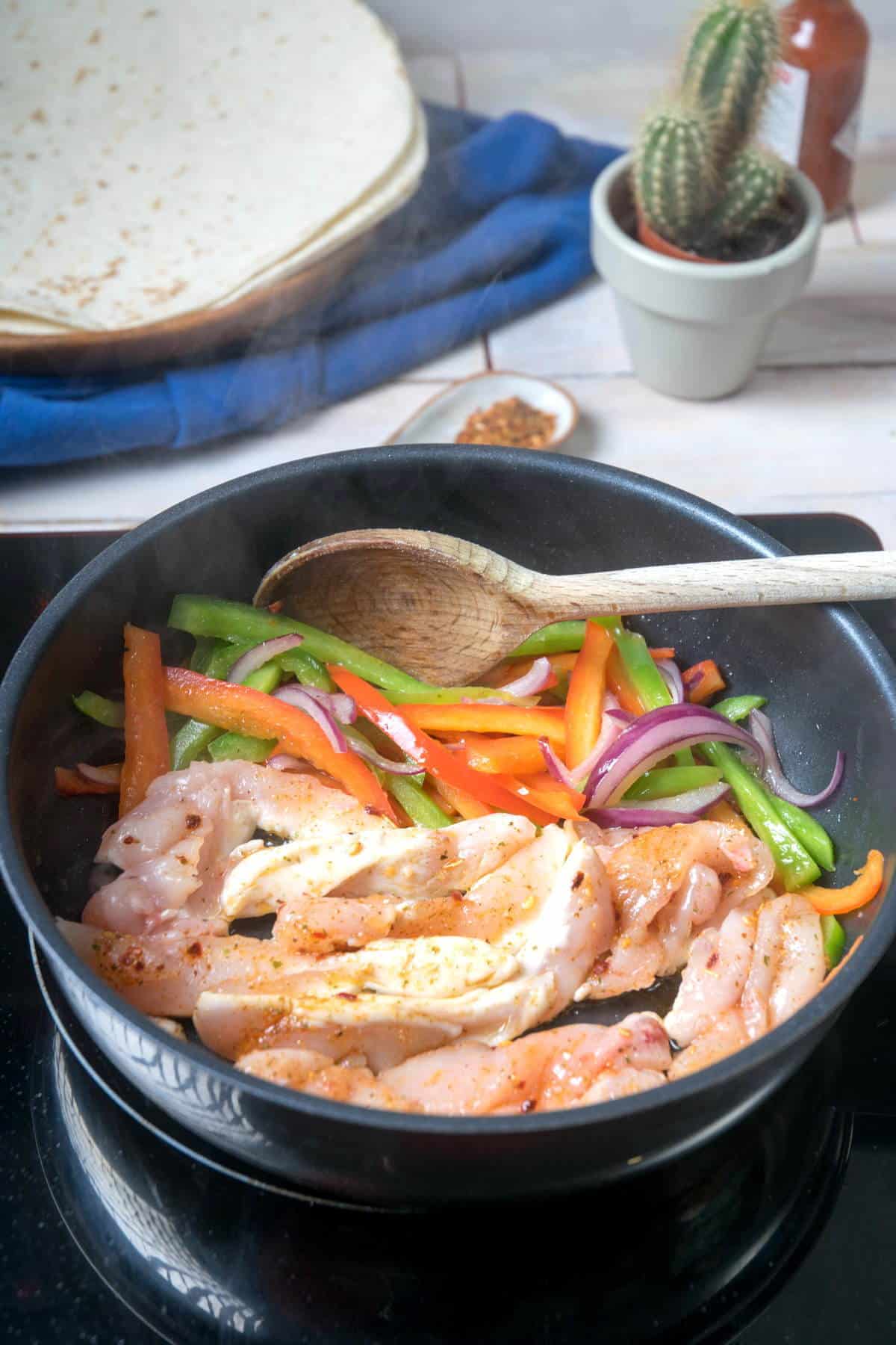 Slice peppers, onions and chicken strips in a frying pan.