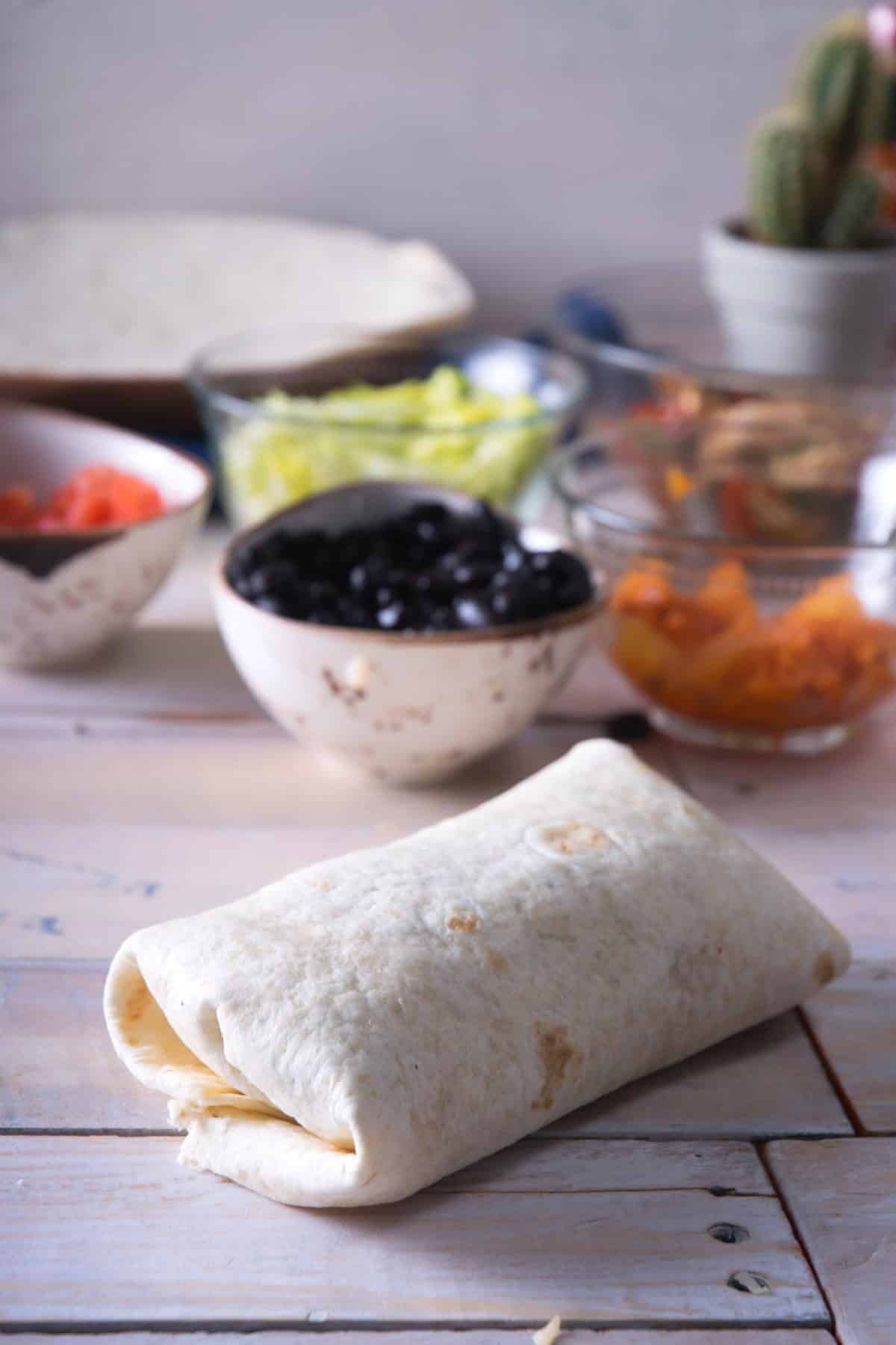Wrapped up uncooked burrito on wooden background.