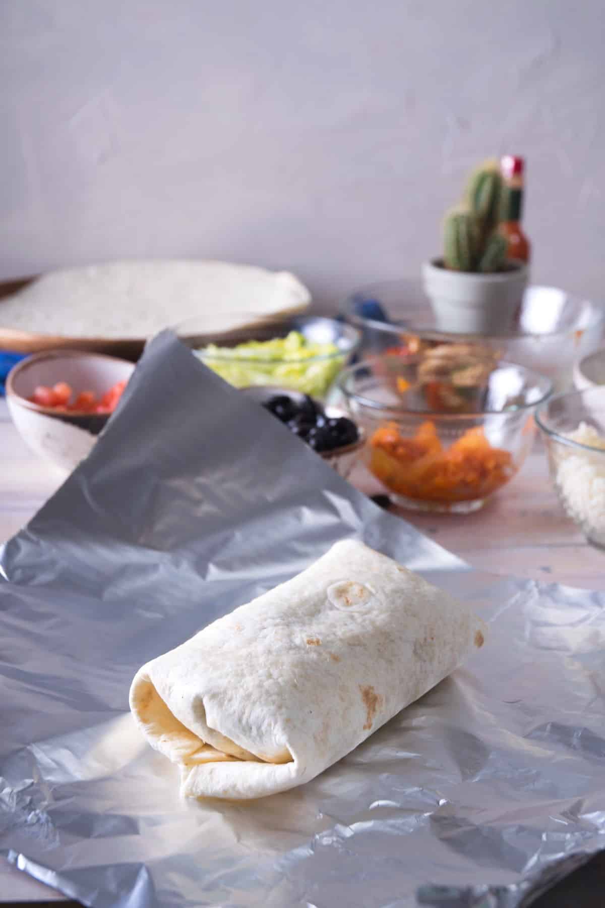 Uncooked burrito on piece of foil.