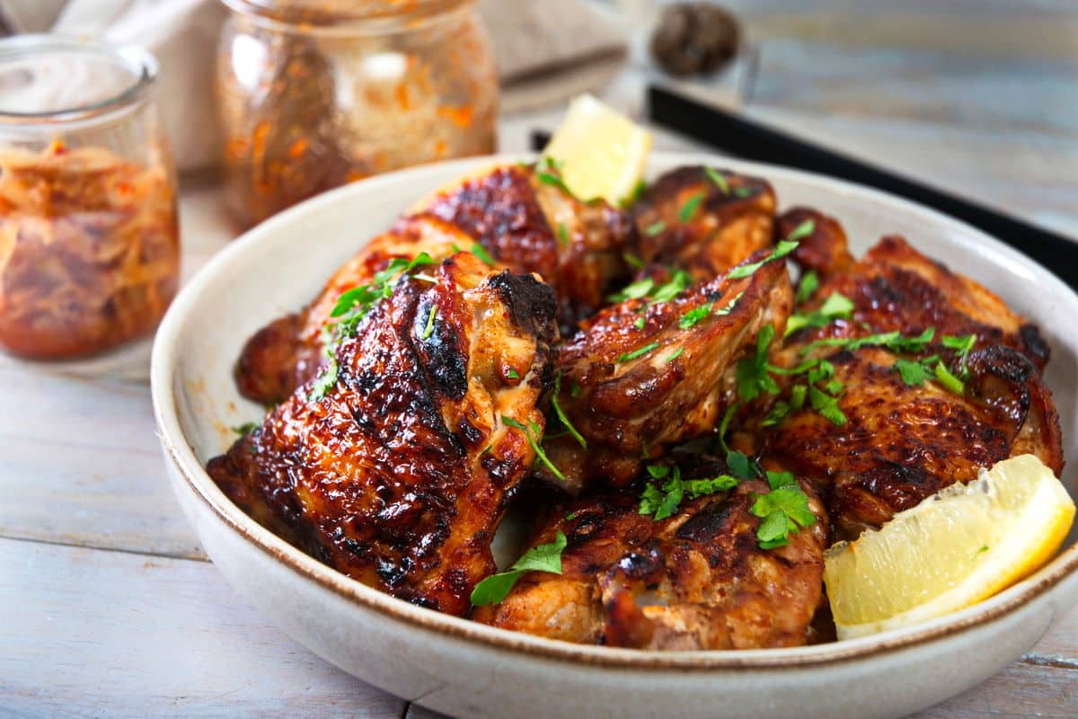 Kimchi chicken thighs in dish with lemon wedges and freshly chopped parsley.