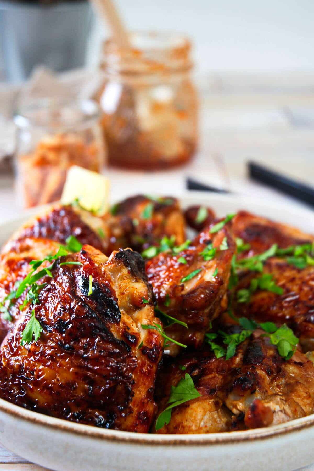 Grilled, caramelized, kimchi chicken thighs in dish with chopped parsley.