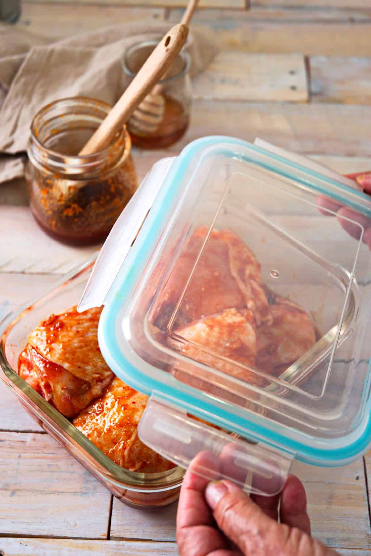 Chicken thighs in a marinade in glass container with lid.