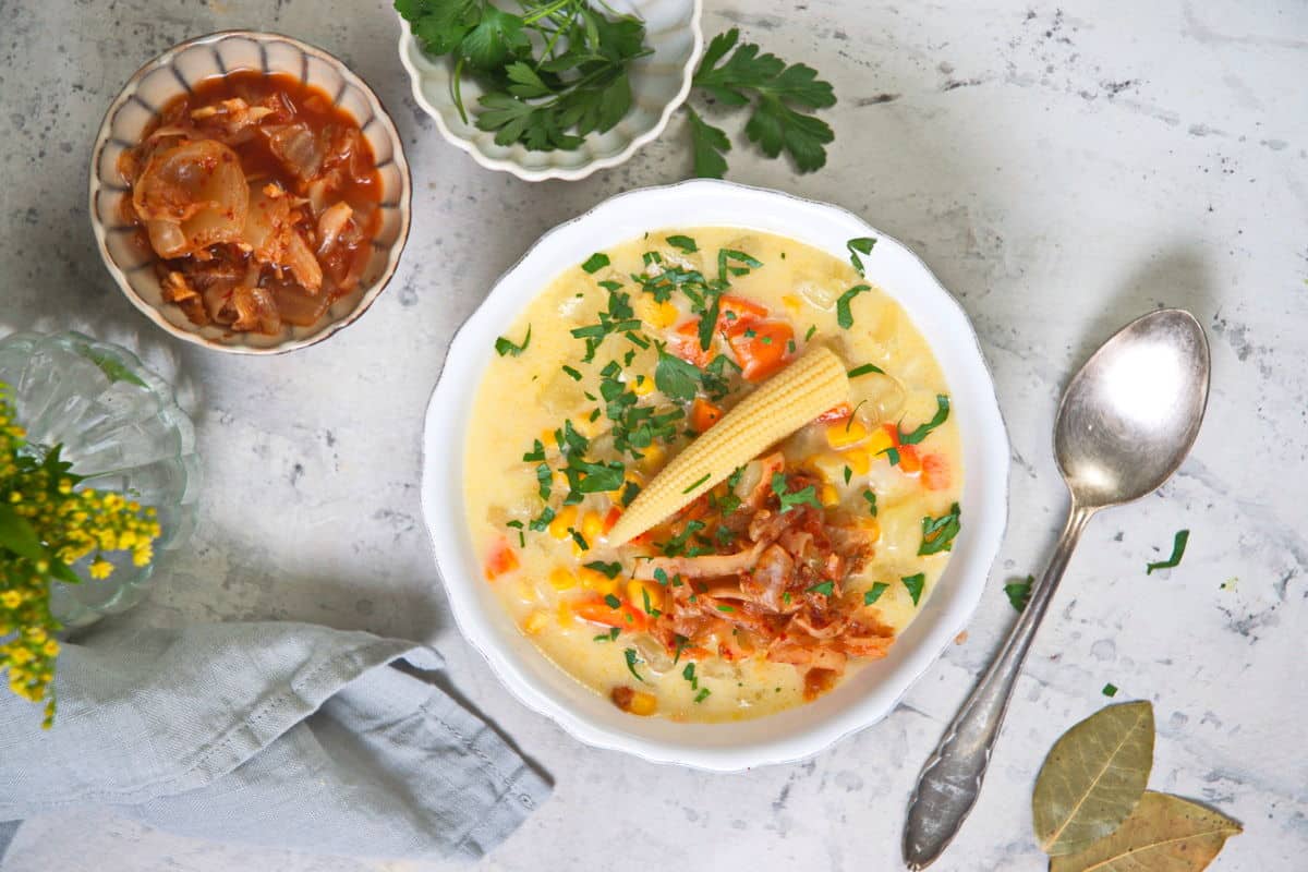 Kimchi chowder in a white bowl with a mini corn on top.
