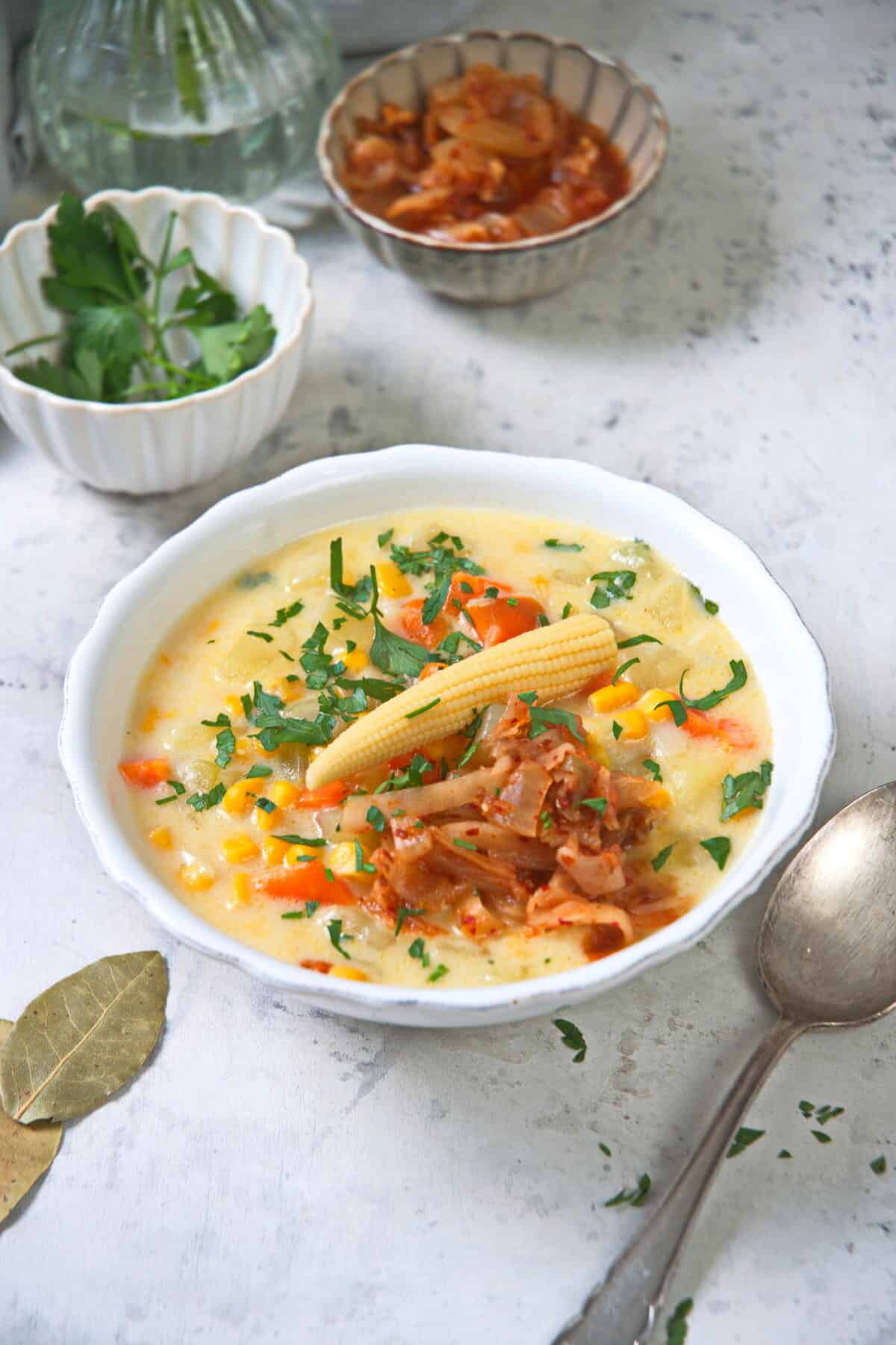Kimchi chowder in a white bowl on light marble background, with a spoon on the side.