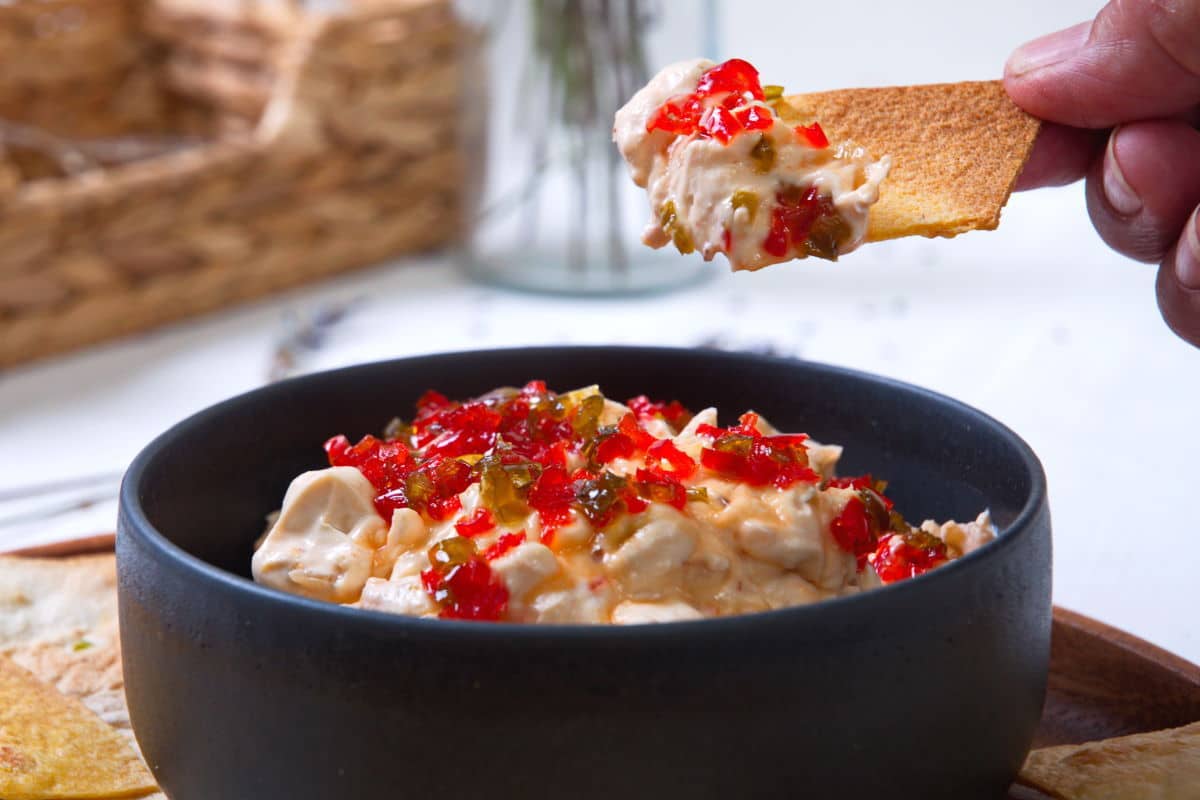 Kimchi cream cheese spread in a small black bowl and on a tortilla chip.
