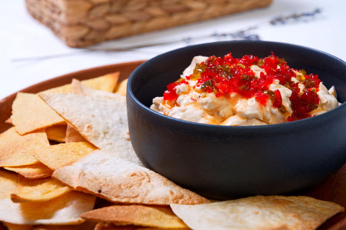Kimchi cream cheese spread in a small black bowl, surrounded by tortilla chips.
