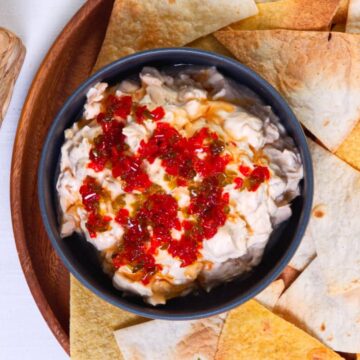Kimchi cream cheese spread in a small black bowl, surrounded by tortilla chips.