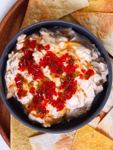 Kimchi cream cheese spread in a small black bowl, surrounded by tortilla chips.