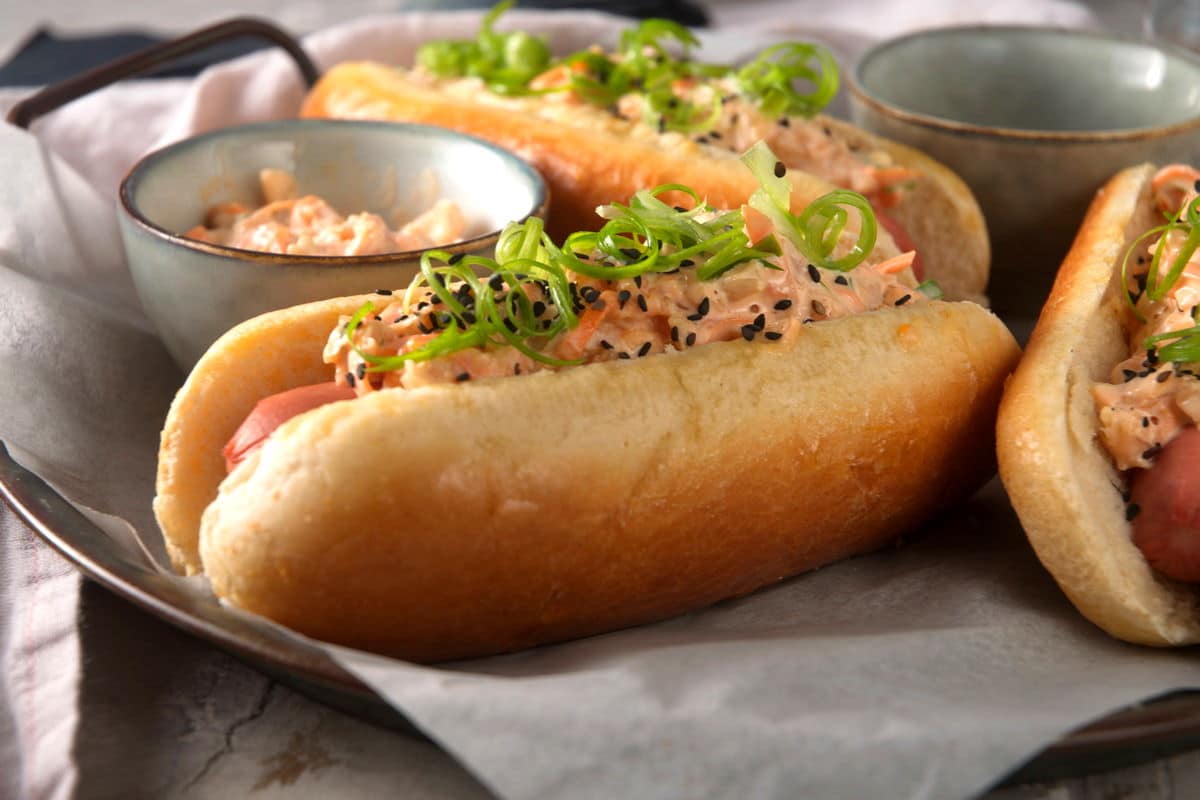 Hot dogs with creamy, kimchi topping, black sesame seeds and sliced green onion curls.