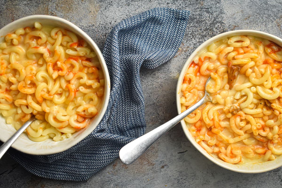 Kimchi mac and cheese in bowls with spoons on blue-grey background.