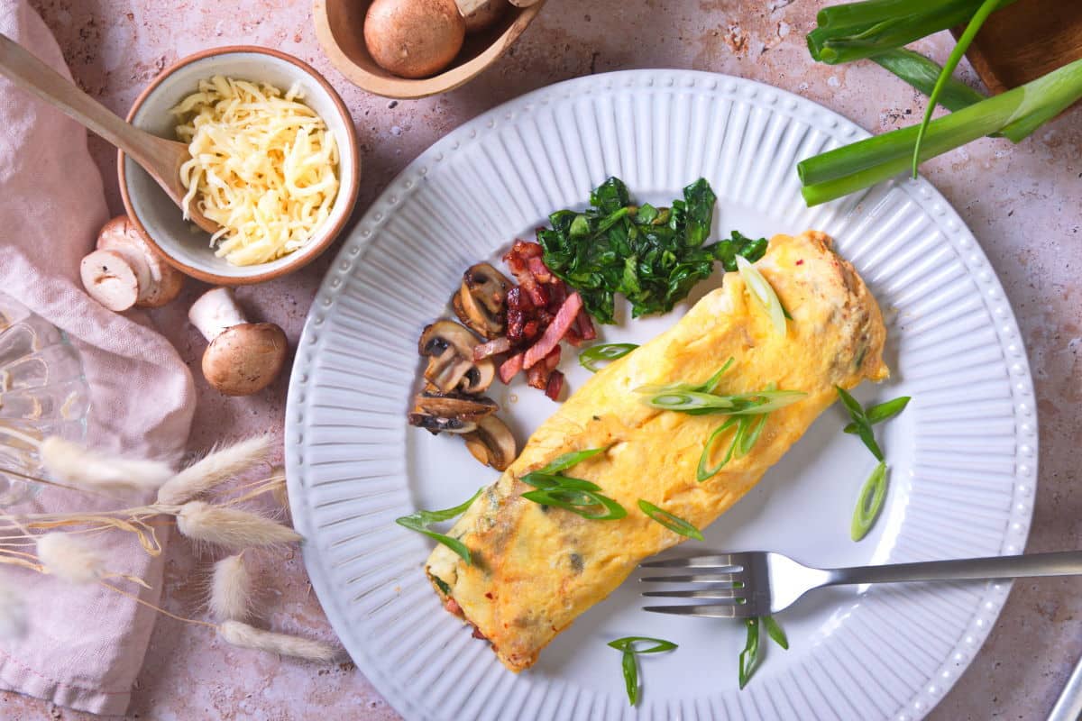 Kimchi omelette on white plate with sliced scallions, grated cheese and mushrooms on the side.