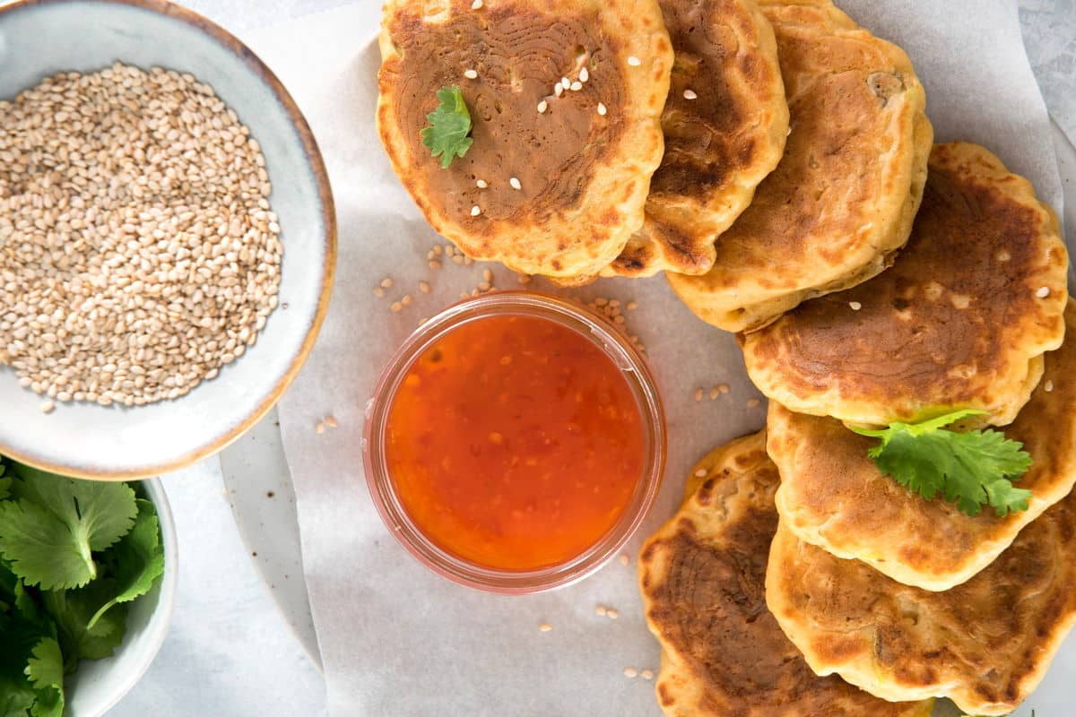 Kimchi pancakes on plate with sweet and sour sauce and sesame seeds.
