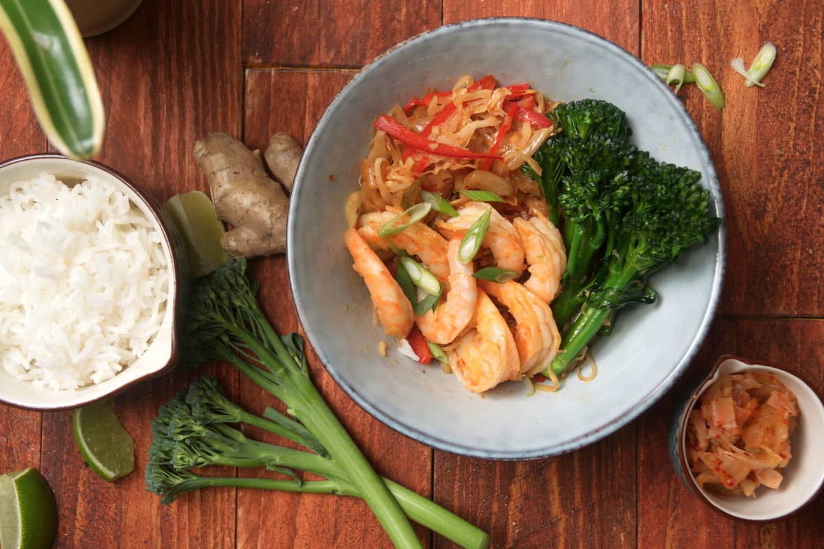 Kimchi and shrimp stir fry over rice in a bowl on wooden background.