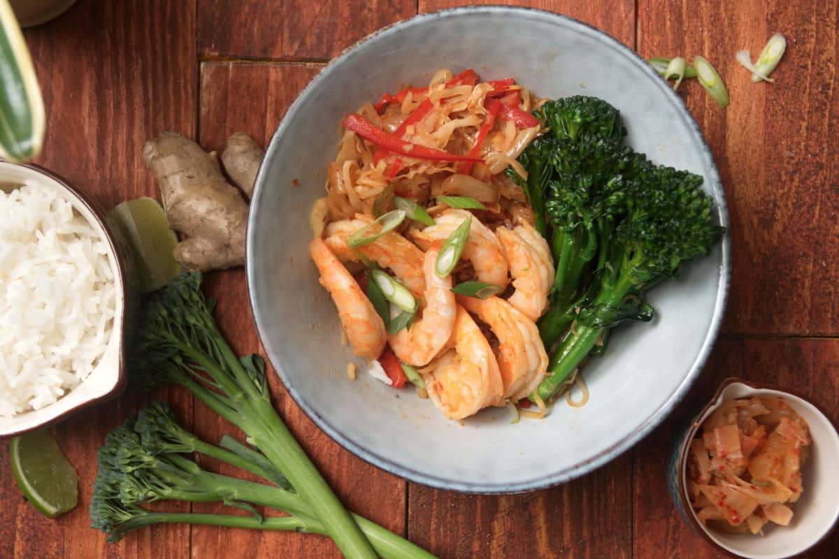 Kimchi and shrimp stir fry over rice in a bowl on wooden background, overhead shot.