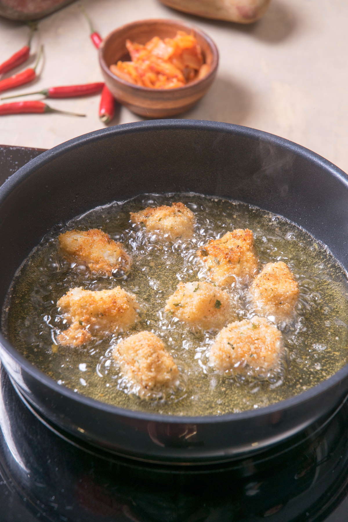 Breaded cod pieces in a frying pan with hot oil.