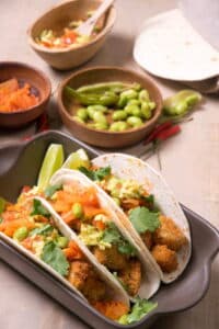 Kimchi and cod tacos in a brown dish, edamame beans in the background.