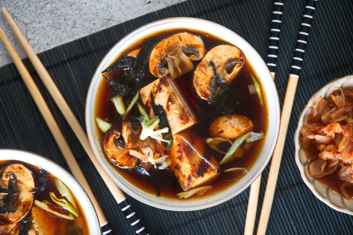Kimchi tofu soup in a bowl on black mat and chopsticks on the side.