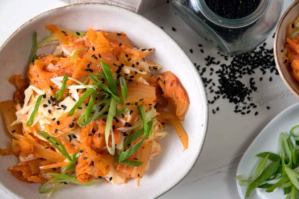 Kimchi slaw in a bowl with sliced scallions and black sesame seeds on the side.